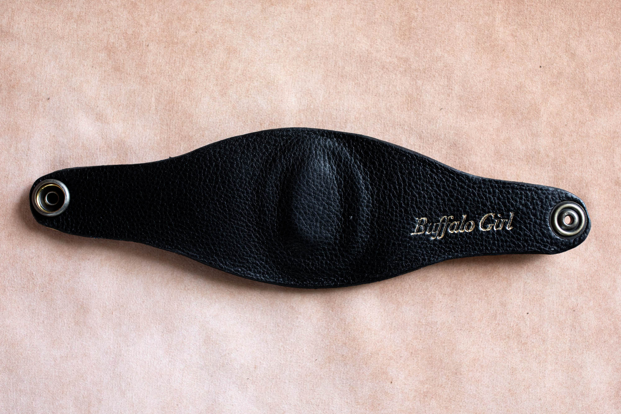 Black leather bracelet with 'Buffalo Girl' branding on a beige background