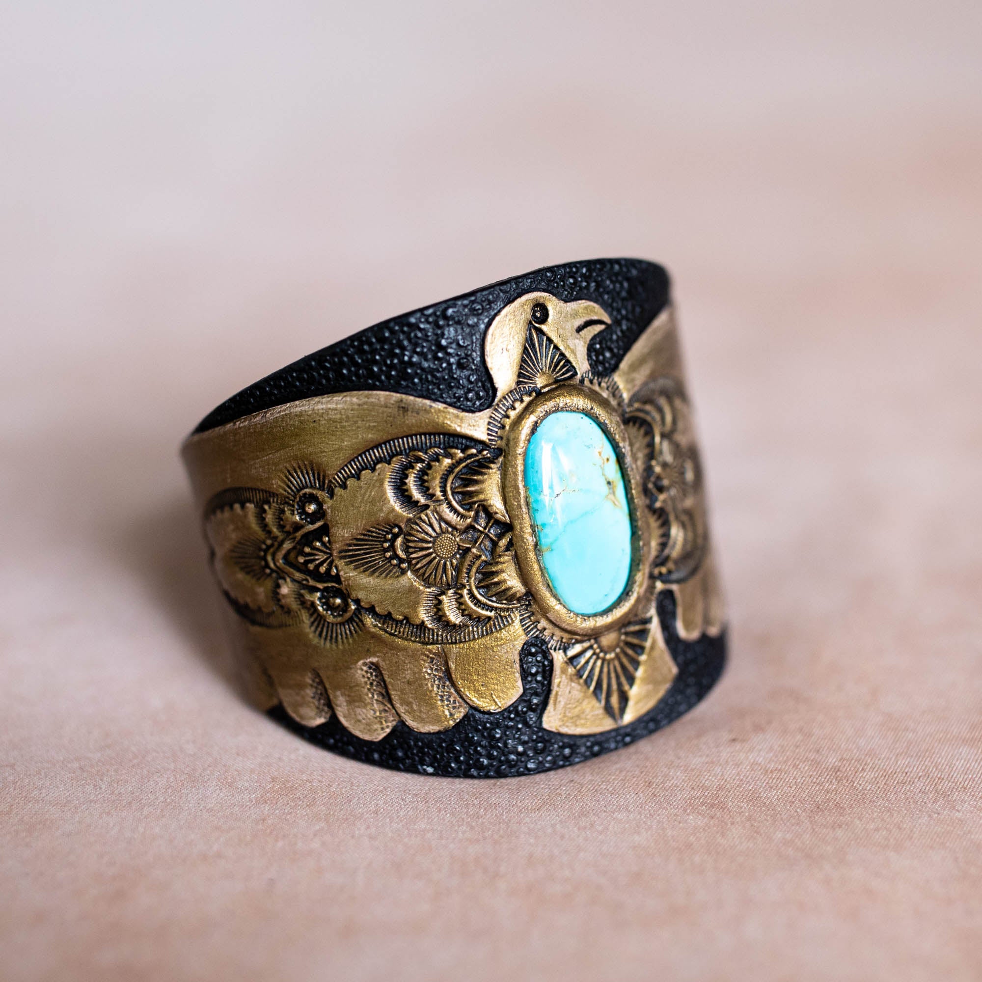 Brass and black cuff bracelet with turquoise stone on a beige background