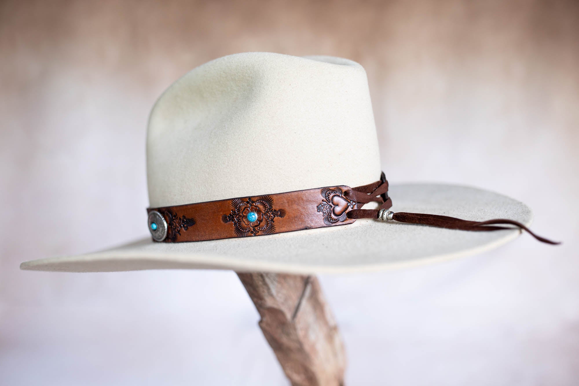 White cowboy hat with a brown leather band featuring metal embellishments on a neutral background