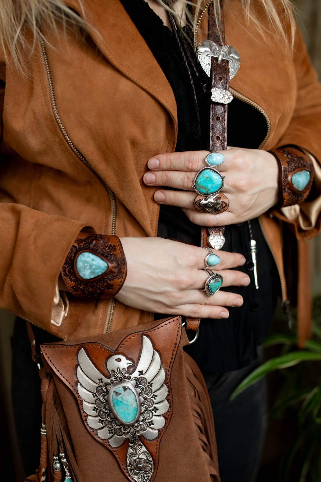 Person wearing turquoise gemstone rings with a brown leather bag featuring similar designs.