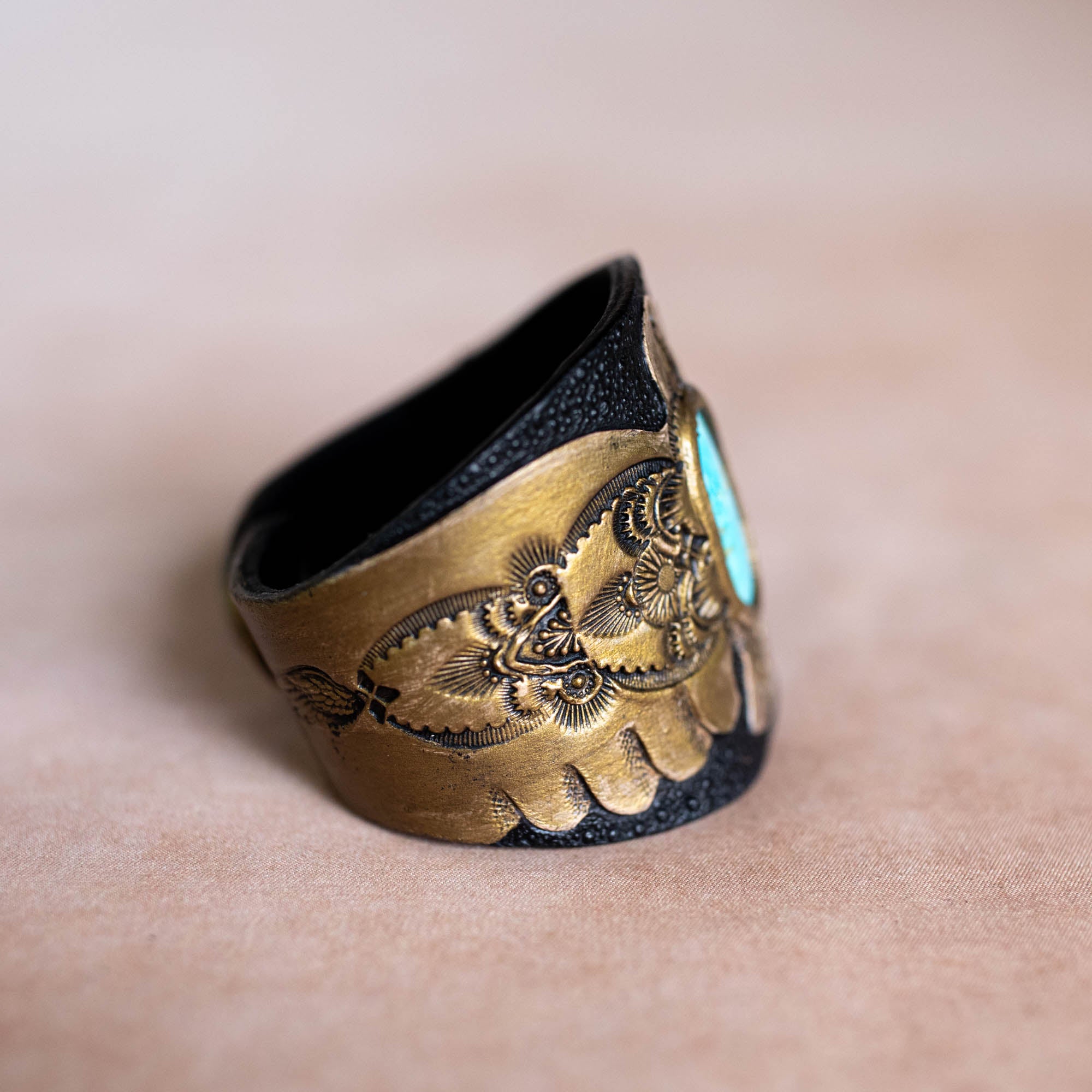 Bronze ring with intricate design and turquoise stone on a beige background